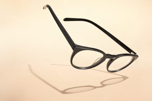 Advertising photo of black glasses with shadow on beige background.