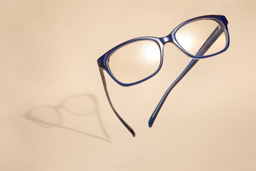 Advertising photo of flying blue glasses with shadow on beige background.