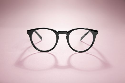 Studio shot of black glasses with long shadow at pink background.