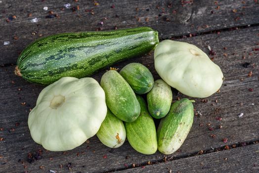 Zucchini, two pattypan squash and few cucumbers harvested from the vegetable garden beds lie on the wooden table