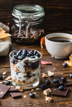 Granola with yogurt, blueberries, honey and chocolate bars. And cup of coffee.