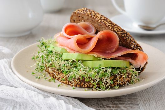 Sandwich of rye bread with cereals, slices of ham and avocado with sprouts of sprouted alfalfa.