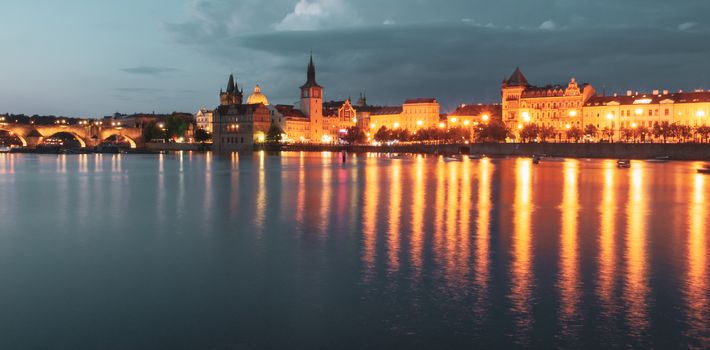 Historical buildings of Smetana Embankment reflected in the water of Vltava River on summer evening. Prague, Czech Republic.