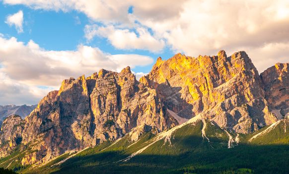 Rocky ridge of Pomagagnon Mountain above Cortina d'Ampezzo with green meadows and blue sky with white summer clouds, Dolomites,, Italy.