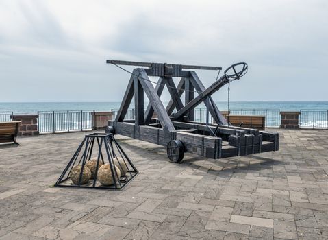 ancient catapult on the ramparts of Alghero ,Sardinia Island, Italy , Defensive wall. Catapult in the downtown of the citywith the sea as background and the big stone bullets in front