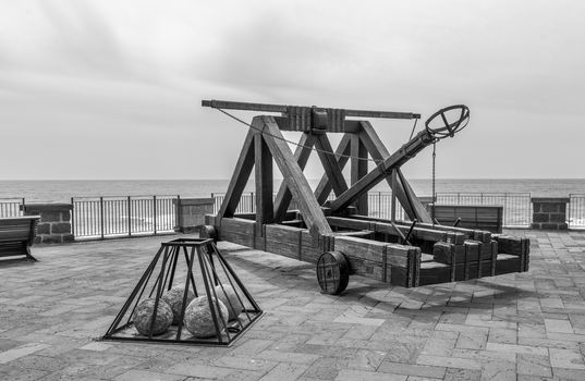 ancient catapult on the ramparts of Alghero ,Sardinia Island, Italy , Defensive wall. Catapult in the downtown of the citywith the sea as background and the big stone bullets in front