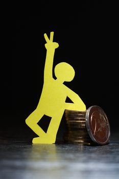 Man made from yellow paper standing near column of coins