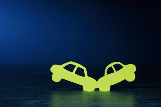 Crush of two cars made from yellow paper on dark background