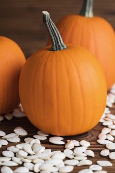 Fresh orange pumpkins and pimpkin seeds close-up on wooden background