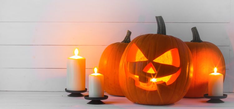 Halloween pumpkin head jack lantern and candles on white wooden background