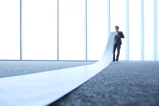 Business man reading very long paper roll in office