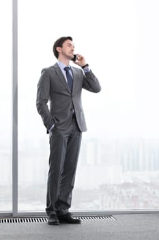 Businessman standing near window, looking at city and talking by phone