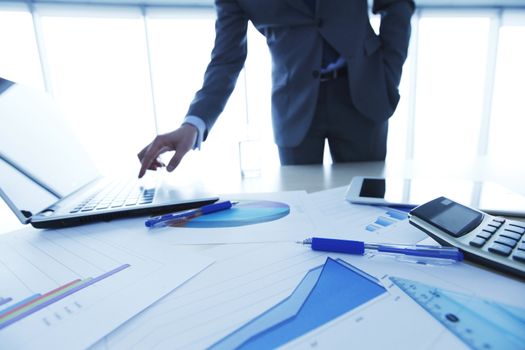 Businessman in office pressing key on laptop, financial data documents on the table