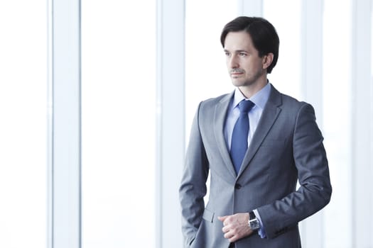 Portrait of handsome businessman standing near windows in office