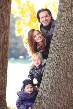 Happy smiling family of parents and children in autumn park standing near big tree trunk