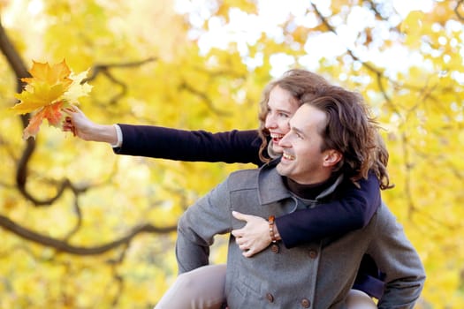 Happy young couple having fun in autumn forest piggyback ride, love, relationships, season and people concept