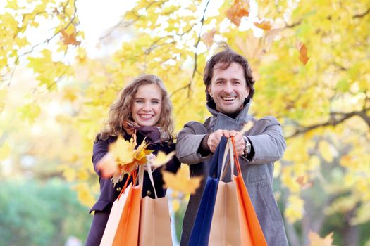 Cheerful couple with shopping bags over autumn trees background