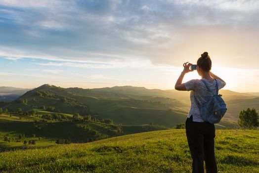 Travel, photo and real life concept - woman taking photo on mobile phone at the mountain peak