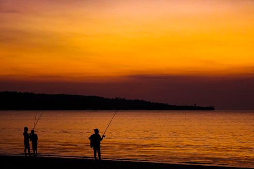 Fishermen catch fish on fishing rods on the beach against the bright sunset. Bali, Indonesia.