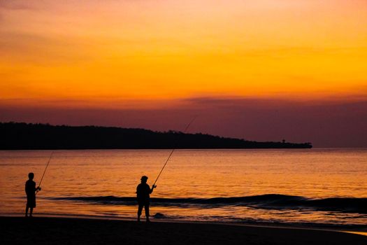 Fishermen catch fish on fishing rods on the beach against the bright sunset. Bali, Indonesia.
