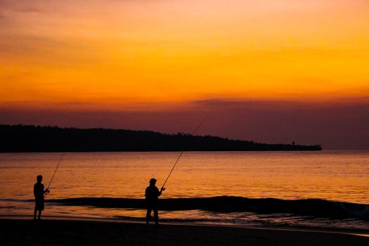 Fishermen catch fish on fishing rods on the beach against the bright sunset. Bali, Indonesia.