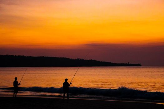 Fishermen catch fish on fishing rods on the beach against the bright sunset. Bali, Indonesia.