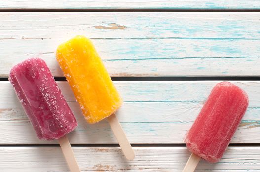 Frozen ice popsicles various flavors on wooden background 