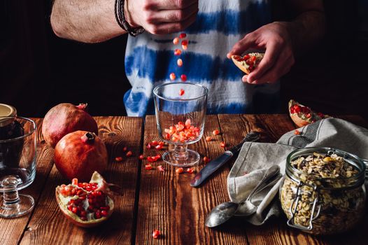 Man Puts Pomegranate Seeds into the Glass. Series on Prepare Healthy Dessert with Pomegranate, Granola, Cream and Jam