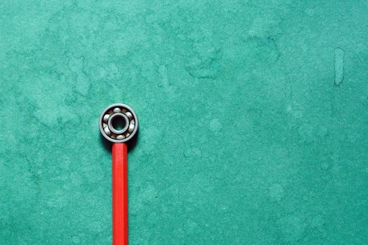 One ball bearing on red pencil against green background