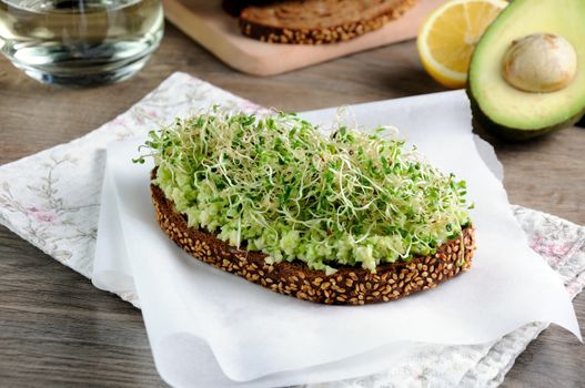 Sandwich of tender, juicy germinated alfalfa and avocado sprouts on slices of rye bread with cereals. This is a great idea for those who watch their health.