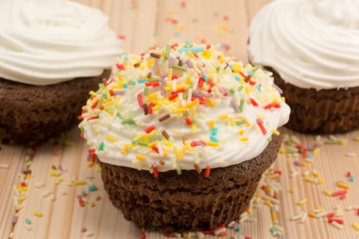 Muffin with cream and colorfull crumbs on top of it sitting on bright wooden table