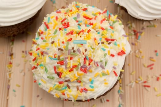 Muffin with cream and colorfull crumbs on top of it sitting on bright wooden table