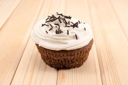 Muffin with cream and chocolate crumbs on top of it sitting on bright wooden table