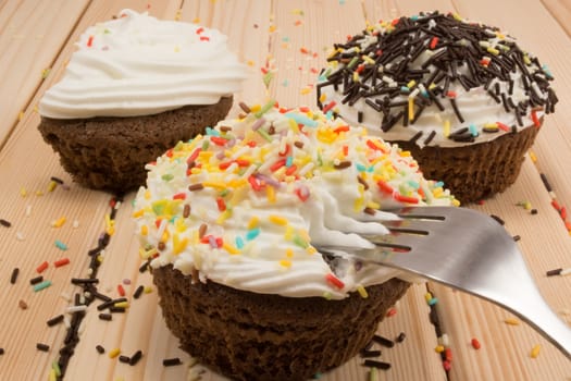 Muffin with cream and crumbs on top of it sitting on bright wooden table. Fork is pinned in muffin