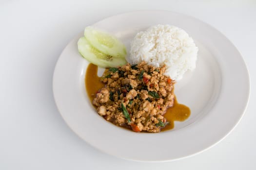Thai Basil Chicken with rice (Pad Krapow) on white plate with cucumber