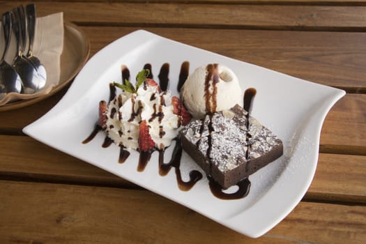 Brownie serve with Strawberry Whip Cream and Vanilla ice cream on plate