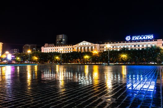 Night city landscape. The main square of the city of Khabarovsk in the light of lanterns, which are reflected in puddles after the rain just passed.