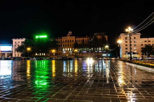Night city landscape. The main square of the city of Khabarovsk in the light of lanterns, which are reflected in puddles after the rain just passed.