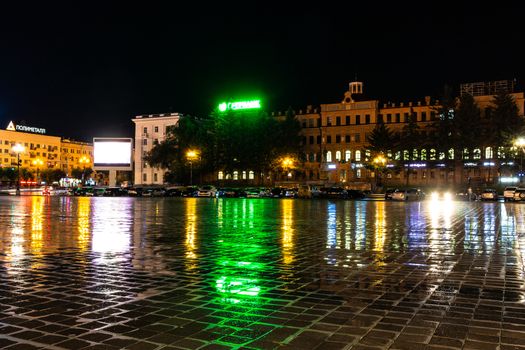 Night city landscape. The main square of the city of Khabarovsk in the light of lanterns, which are reflected in puddles after the rain just passed.