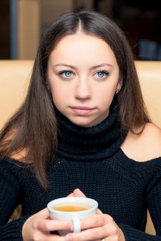 Cute brunette with a cup of tea in a cafe in a black sweater