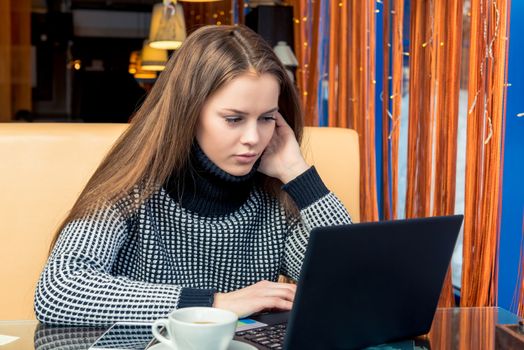 Young beautiful woman in a cafe working with laptop and drinking coffee