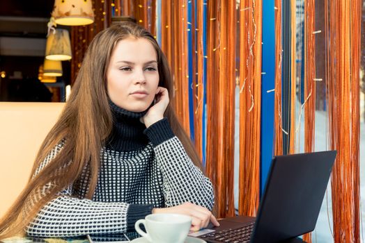 Beautiful young girl in cafe working with laptop and drinking coffee