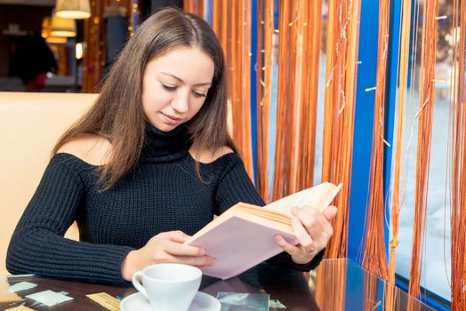 Smart beautiful girl with a book at a table in a cafe