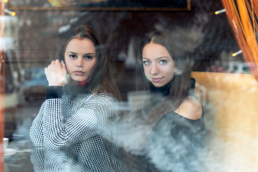 Portrait of young beautiful girlfriends in a cafe, shooting behind a glass