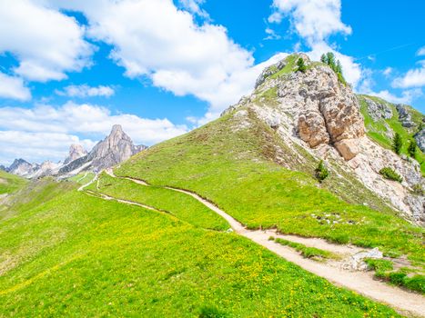 Landscape of Dolomites with green meadows, blue sky, white clouds and rocky mountains.