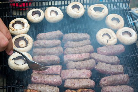 Grilling cevapi and mushrooms. Smoke visible. Upper angle