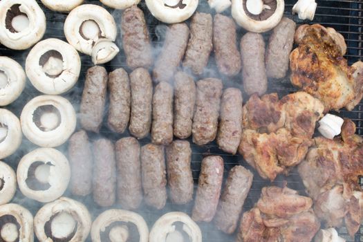 Grilling cevapi and mushrooms. Smoke visible. Upper angle