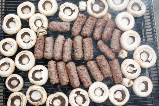 Grilling cevapi and mushrooms. Smoke visible. Upper angle