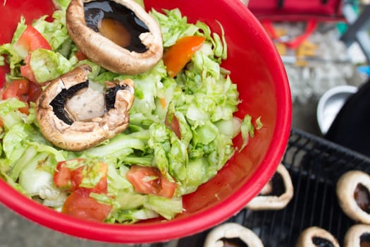 Ball filled up with fresh salad and grilled mushrooms. Barbecue visible in the background