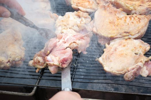 Turning over raw pork chops on grill. Smoke rising from heated grill